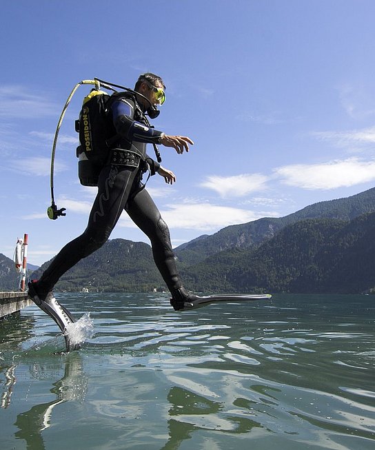 Taucher springt vom Steg in den See