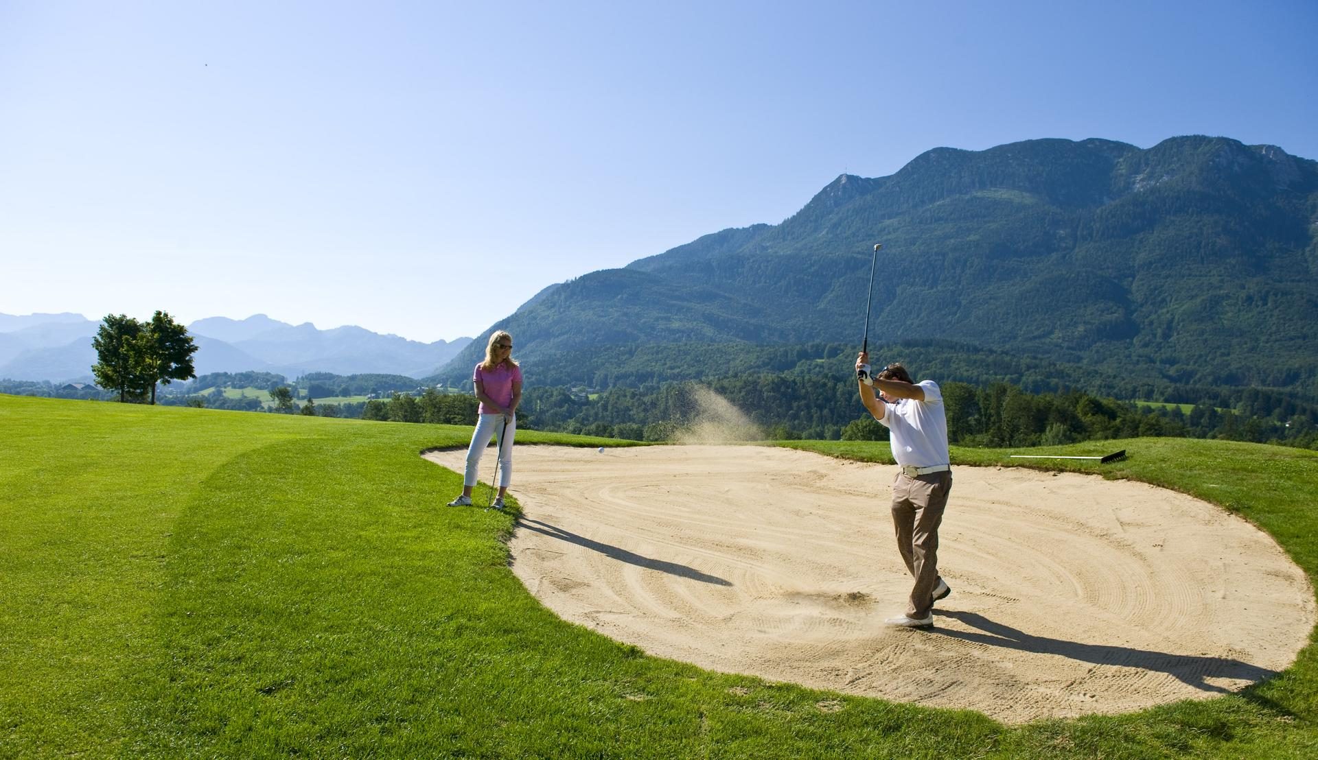 Golferin beim Abschlag mit grünen Bergen und blauem Himmel im Hintergrund