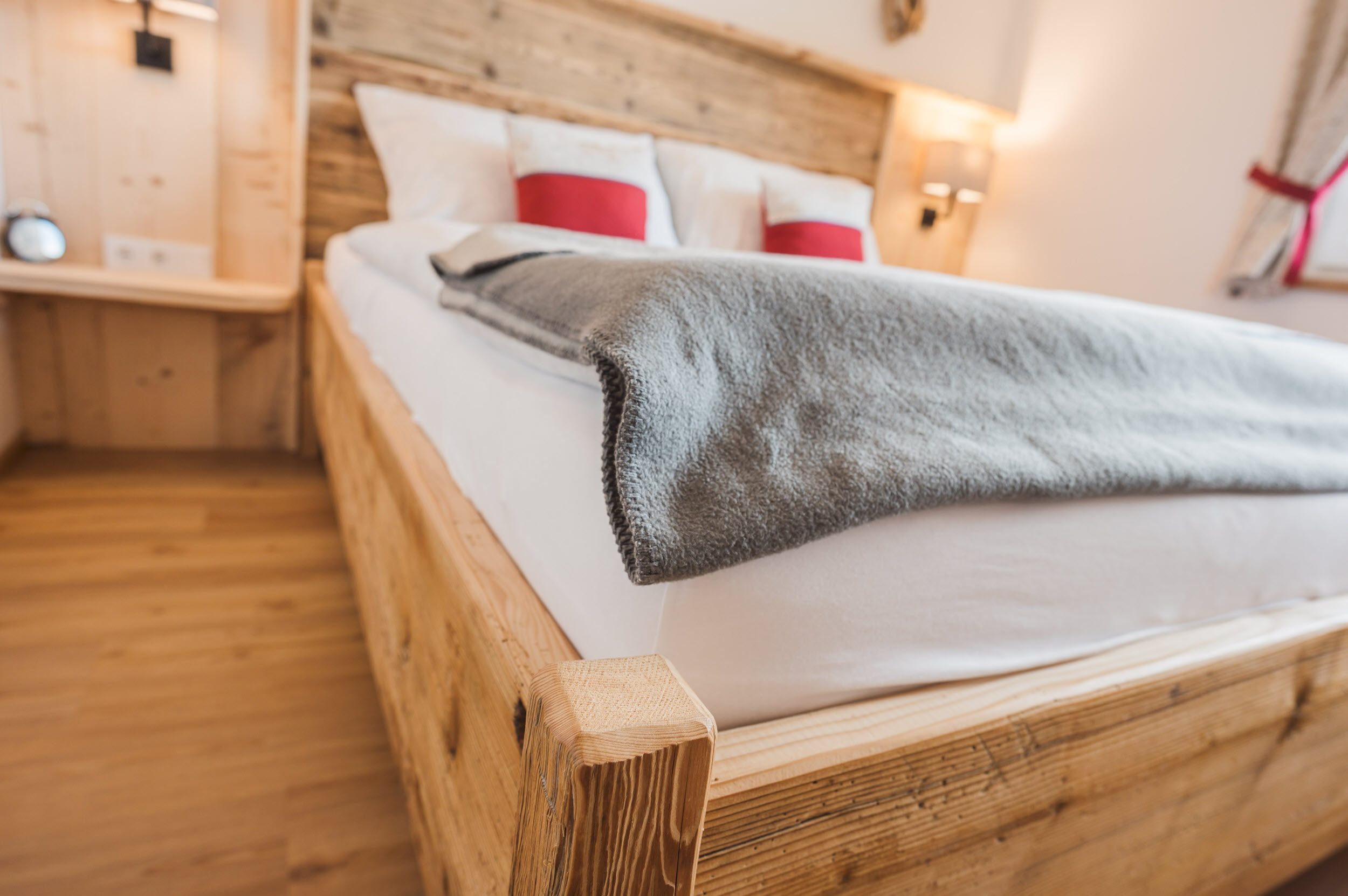 Schlafzimmer 1 Bett-Detail mit Altholz-Kopfteil und roten Kissen