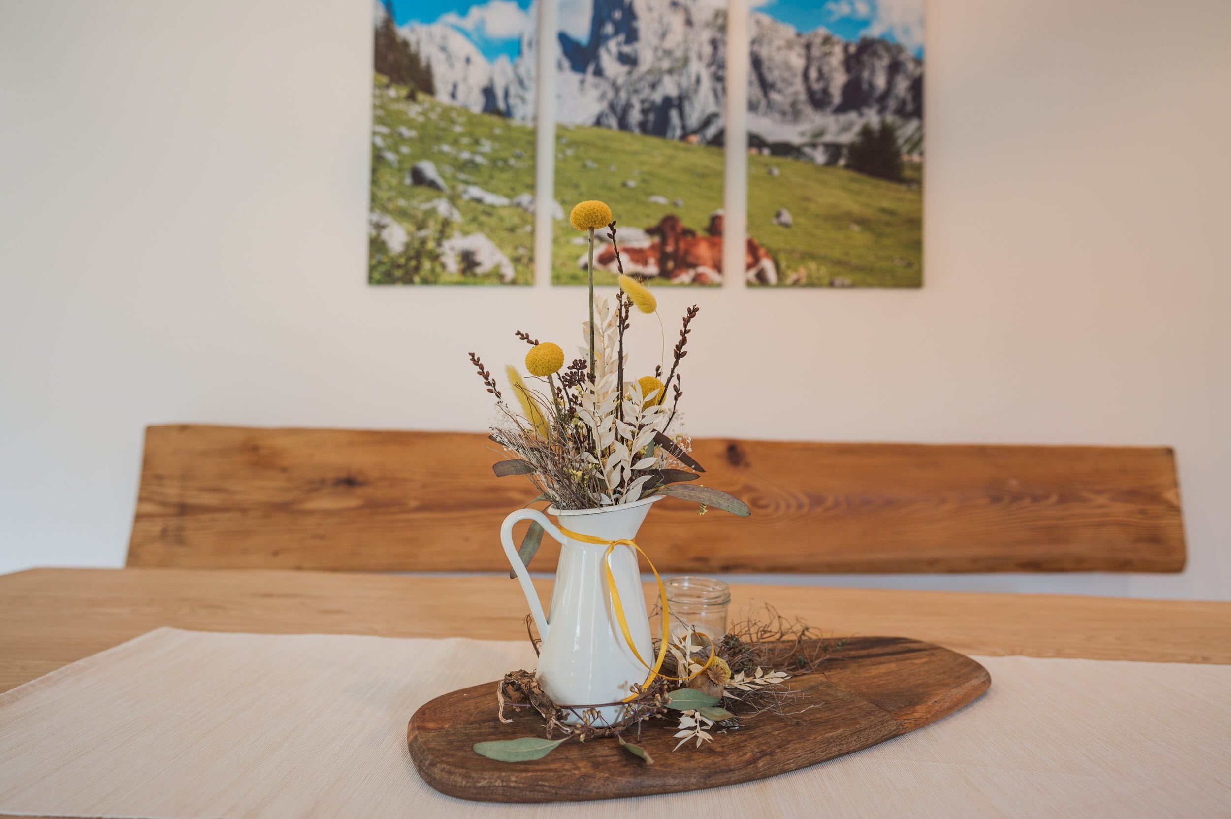 Esstisch-Detail mit Trockenblumen und Almpanorama-Bild